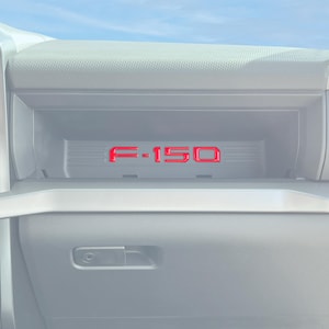 May include: A close-up of the interior of a vehicle, showing a gray dashboard with a red "F-150" logo in a storage compartment.