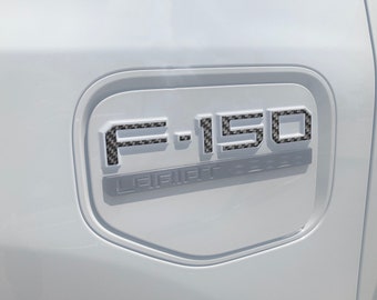 Könnte beinhalten: Ein weißer LKW mit einem schwarzen F-150-Emblem aus Kohlefaser auf der Rückseite. Das Emblem trägt den Text "LARIAT" unter den Zahlen.