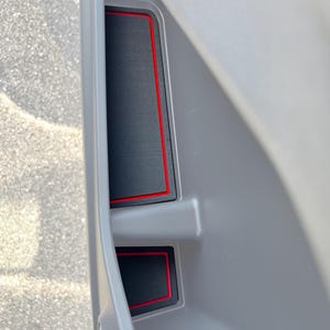 Könnte beinhalten: Zwei schwarze Autotür-Organizer mit rotem Besatz. Die Organizer sind aus einem strukturierten Material gefertigt und haben eine rechteckige Form.