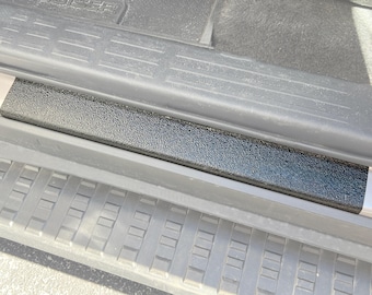 May include: A close-up of a black textured car door sill protector. The protector is installed on a gray car door sill.