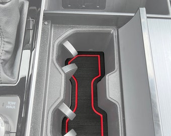 May include: A black car interior with a red trim around a black rubber mat in a center console compartment.