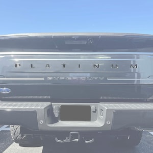 May include: Rear view of a black Ford F-Series Super Duty pickup truck with a chrome tailgate and the word "PLATINUM" in silver lettering on the tailgate.