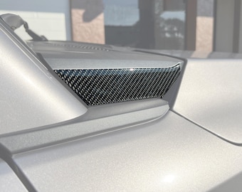 May include: A close-up of a silver car with a black carbon fiber vent on the side. The vent is a decorative piece that adds a sporty look to the car.