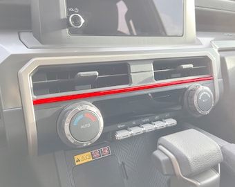 May include: Close-up of a car's dashboard with a red trim, a silver knob labeled "AUTO", and a row of buttons labeled "TWEETER", "MODE", "CD", and "AUX".