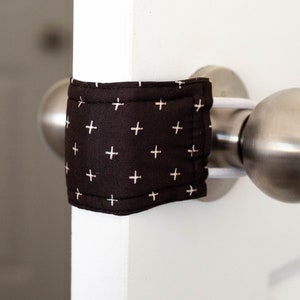 May include: A white door with a silver door handle and a black and white patterned fabric door stop.