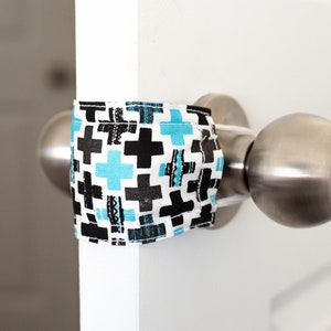 May include: A white door with a silver door handle. A blue, black and white patterned fabric is wrapped around the door handle to prevent it from opening.