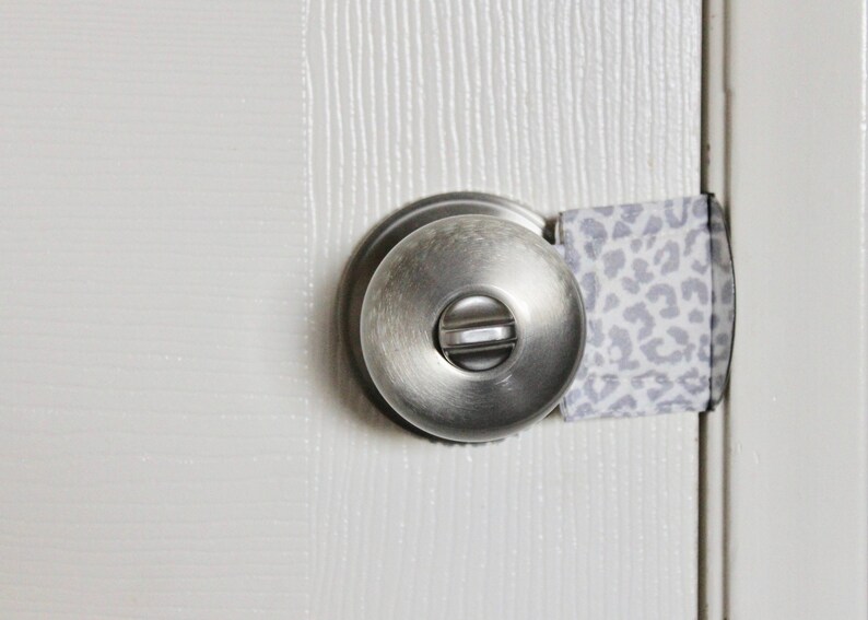 Puede incluir: Un pomo de puerta plateado con una tela de patr&oacute;n blanco y gris envuelta alrededor para evitar que la puerta se abra.