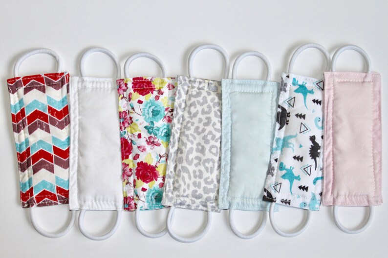 Puede incluir: Siete mascarillas de tela para la cara con lazos el&aacute;sticos blancos para las orejas. Las mascarillas presentan diferentes patrones, incluyendo un chevron rojo y blanco, un patr&oacute;n floral blanco, un estampado de leopardo gris, un color s&oacute;lido azul claro, un patr&oacute;n blanco con dinosaurios negros y un color s&oacute;lido rosa.