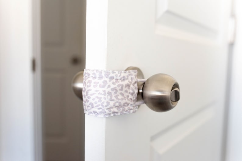 Puede incluir: Una puerta blanca con una perilla de puerta plateada. Una tela con estampado blanco y gris est&aacute; envuelta alrededor de la perilla de la puerta para evitar que se abra.