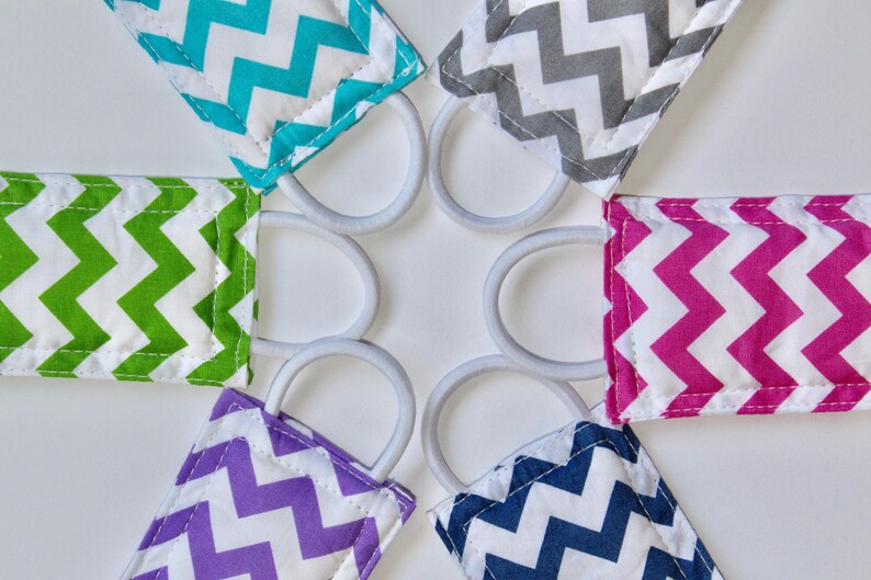 Puede incluir: Seis gomas para el pelo de tela de colores con un patr&oacute;n de chevron en turquesa, verde, rosa, morado, azul marino y gris. Las gomas para el pelo est&aacute;n dispuestas en c&iacute;rculo sobre un fondo blanco.