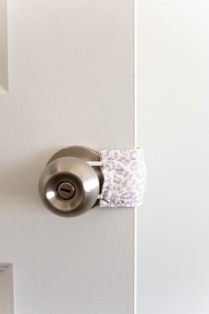 Puede incluir: Una puerta blanca con una perilla de puerta plateada y un tope de puerta de tela blanca y gris con estampado.