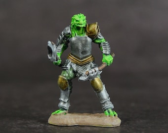 May include: A green and silver painted miniature figurine of a lizard person wearing armour and holding a weapon.