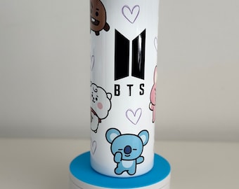May include: White stainless steel tumbler with a black BTS logo and cartoon characters. The tumbler has a blue lid and a straw.