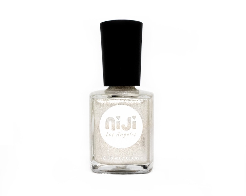 Puede incluir: Una botella de vidrio transparente de esmalte de u&ntilde;as con purpurina plateada con una tapa negra. La botella tiene una etiqueta blanca con el texto "Niji Los Angeles" y "0.5 oz" impreso en ella.