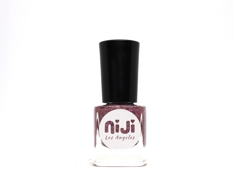 Puede incluir: Una botella de esmalte de u&ntilde;as de purpurina rosa con una tapa negra. La botella tiene una etiqueta blanca con el texto "niji Los Angeles".