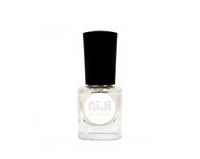 Puede incluir: Una botella de vidrio transparente de esmalte de u&ntilde;as con un acabado de brillo plateado. La botella tiene una tapa negra y una etiqueta blanca con el texto "niji los angeles" en ella.