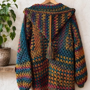May include: A long-sleeved hooded cardigan featuring a multi-colored granny square crochet pattern in shades of teal, mustard yellow, magenta, and dark blue. The garment includes a hood with a decorative yarn tassel hanging from the center back.