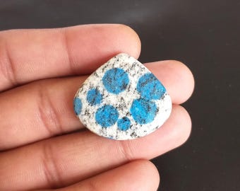 May include: A triangular-shaped stone with a white and gray speckled background and vibrant blue circular patterns. The stone is held in a hand, showcasing its unique color and texture. This natural stone is ideal for jewelry making or collecting.