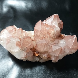 May include: A cluster of translucent, pale pink quartz crystals with sharp, pointed terminations. The mineral formation features a mix of clear and reddish-tinted crystalline structures growing from a central base, displaying natural geometric facets.