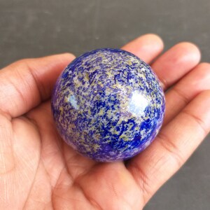 May include: A polished, blue and gold lapis lazuli sphere. The sphere has a smooth, round surface and is speckled with gold pyrite.