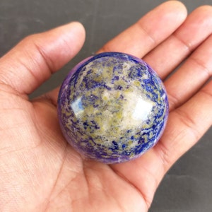 May include: A polished, blue, purple, and gold lapis lazuli sphere. The sphere is smooth and has a high gloss finish.