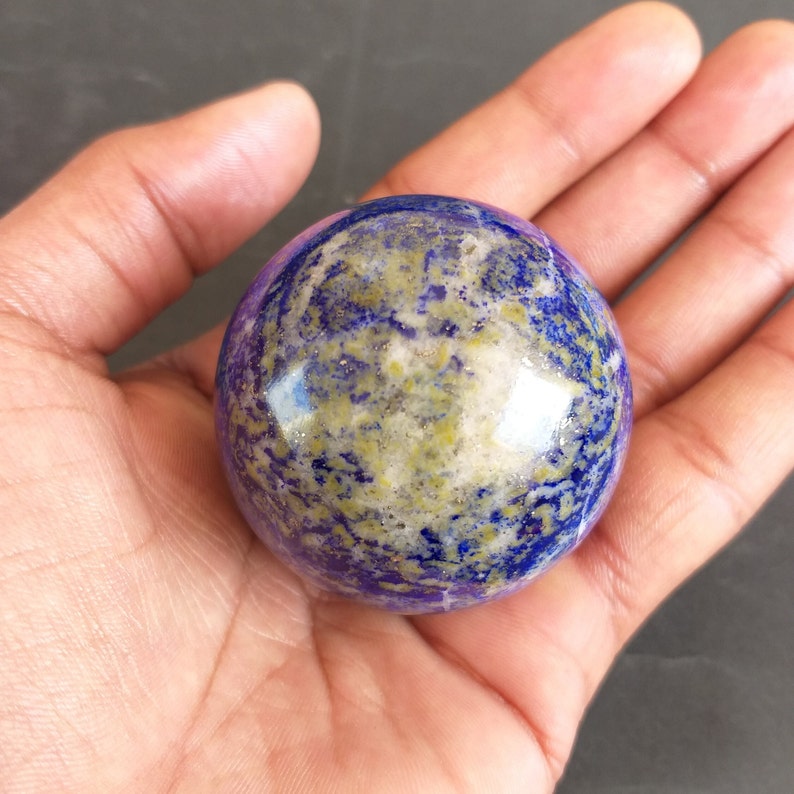 May include: A polished, blue, purple, and gold lapis lazuli sphere. The sphere is smooth and has a high gloss finish.