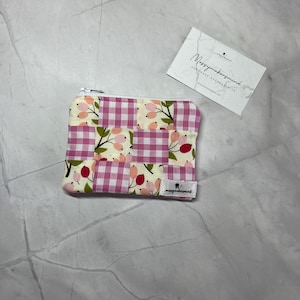 Könnte beinhalten: Ein kleiner, quadratischer Münzbeutel mit Reißverschluss und Patchwork-Design. Die Tasche hat einen Mix aus rosa Vichy- und floralem Stoff. Ein kleines Etikett mit dem Text "messymakersmind" ist angebracht. Eine Visitenkarte ist ebenfalls vorhanden.