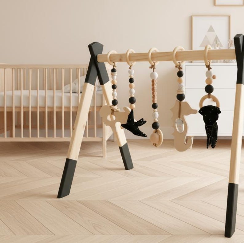 May include: A wooden baby play gym with hanging toys. The frame is natural wood with black accents. Hanging toys include wooden beads, a seahorse, a bird, and a seahorse-shaped teether. The background includes a crib and a dresser.