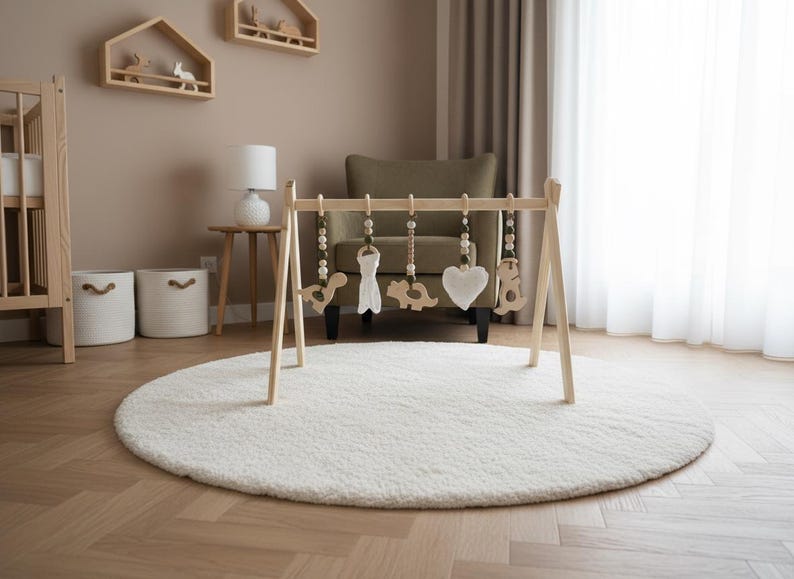 May include: A wooden baby gym with hanging toys, including a heart, dinosaur, and bear, sits on a white, round rug. The room features a crib, shelves, and a chair, all in neutral tones, creating a calming nursery environment.
