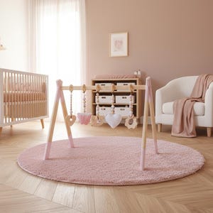 May include: A nursery scene with a white crib, a wooden baby gym with hanging toys, and a pink rug. The room has a neutral color palette with a white armchair and a wooden floor.