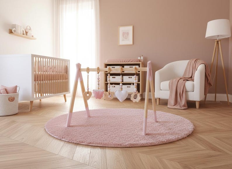 May include: A nursery scene with a white crib, a wooden baby gym with hanging toys, and a pink rug. The room has a neutral color palette with a white armchair and a wooden floor.