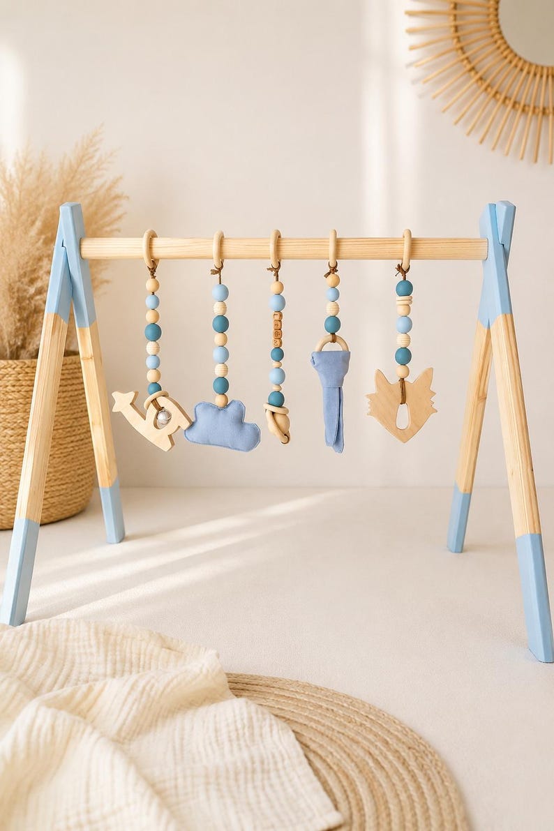 May include: Wooden baby play gym with blue accents and hanging toys. The toys include a wooden airplane, a blue cloud, a wooden bear, a blue key, and a wooden fox. The wooden frame has blue painted legs and a natural wood top.
