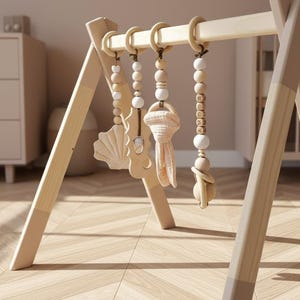May include: Wooden baby play gym with hanging toys. The frame is light-colored wood with a natural finish. Hanging toys include a wooden seashell, a fabric toy, and wooden beads. The gym is set on a light wood floor.