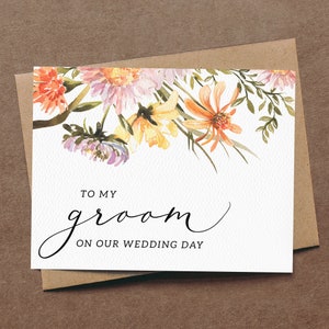 May include: A white card with a watercolor floral design in shades of orange, yellow, and purple. The card says "To my groom on our wedding day".