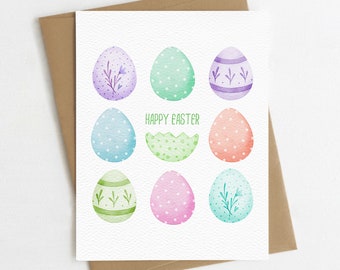 May include: A white card with the text "Happy Easter" in green lettering. Nine watercolor Easter eggs are arranged in a 3x3 grid. The eggs are decorated with various patterns, including polka dots, stripes, and floral designs. The eggs are in shades of purple, blue, green, pink, and orange.