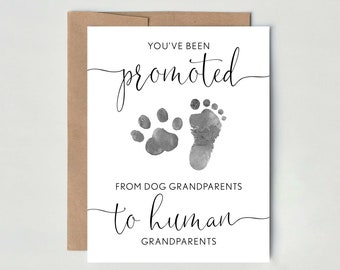 May include: A white card with black text that reads "You've been promoted from dog grandparents to human grandparents". The card features a watercolour illustration of a paw print and a baby footprint.