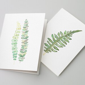 May include: Two watercolor greeting cards with green foliage designs. One card features three sprigs of green leaves, while the other card has a single fern leaf.