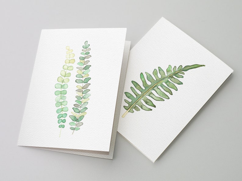 May include: Two watercolor greeting cards with green foliage designs. One card features three sprigs of green leaves, while the other card has a single fern leaf.