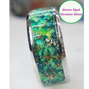 May include: A silver ring with a green opal and gold flecks embedded in the band. The ring is labeled "Green Opal German Glass".