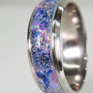 May include: A silver ring with a blue and iridescent inlay. The inlay is made of small pieces of glass or stone.