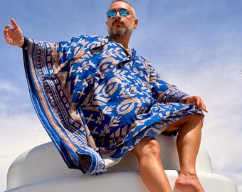 May include: A loose-fitting blue kaftan featuring a repeating tan-colored botanical and geometric pattern. The garment has wide sleeves, a V-neckline, and a decorative border along the edges, showcasing a vibrant contrast between the blue and tan.