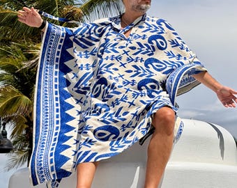 May include: A loose-fitting kaftan featuring a bold blue and white pattern with geometric shapes, stylized leaves, and paisley motifs. The garment has a wide V-neckline, short sleeves, and a decorative border along the edges with intricate patterns.