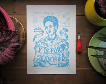 Puede incluir: Una impresión linograbada azul y blanca de Frida Kahlo con una pancarta que dice "F is for Feminism".