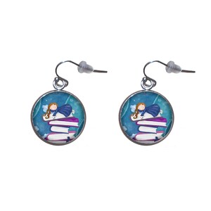 Puede incluir: Un par de pendientes de plata con una ilustración azul y blanca de un hada durmiendo sobre una pila de libros. El hada lleva un vestido azul y tiene el pelo largo y castaño.