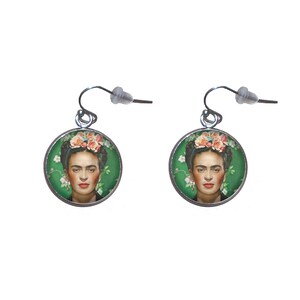 Könnte beinhalten: Ein Paar silberne Ohrringe mit runden, grünen und weißen Blumenmotiven, die ein Porträt von Frida Kahlo zeigen.