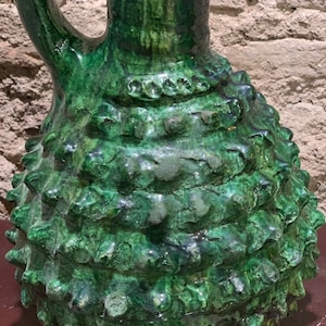 Może przedstawiać: Zielony dzban ceramiczny z fakturowaną, kolczastą powierzchnią i uchwytem. Dzban ma zieloną glazurę z lekko opalizującym wykończeniem.
