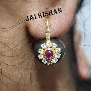 May include: Gold earrings with a round, black stone set with a pink gemstone and white diamonds. The earrings have a hook closure.