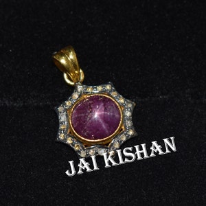 May include: A gold pendant with a star-shaped setting featuring a red ruby gemstone surrounded by smaller diamonds. The pendant is on a black background with the text "JAI KISHAN" visible below.