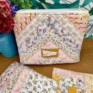 Peut inclure: Un ensemble de disques démaquillants réutilisables dans une variété de motifs floraux, y compris rose, blanc et or. Les disques sont emballés dans une pochette zippée blanche avec un design patchwork représentant des ananas, des oiseaux et des motifs floraux. La pochette porte une étiquette qui indique "Back to the Nature".