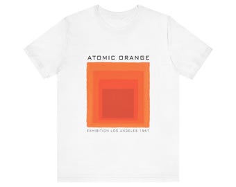 May include: A white short-sleeve t-shirt featuring a graphic of nested orange squares in varying shades. The text ATOMIC ORANGE is printed above the graphic, and the text EXHIBITION LOS ANGELES 1967 is printed below the graphic in black lettering.